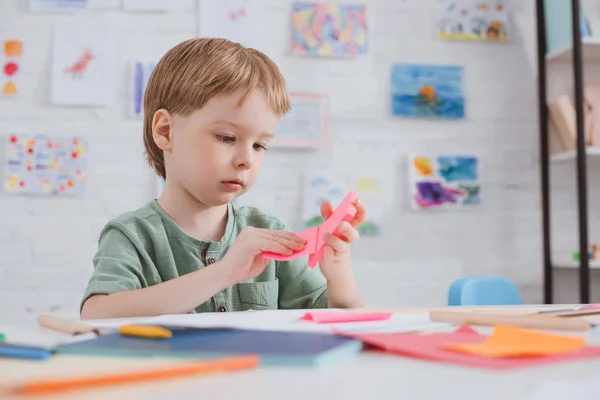 Carino bambino in età prescolare con carta rosa seduto a tavola in classe — Foto stock