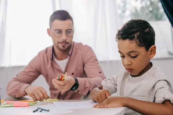 Kaukasischer Lehrer und afrikanisch-amerikanischer Junge zeichnen gemeinsam Bild im Klassenzimmer — Stockfoto