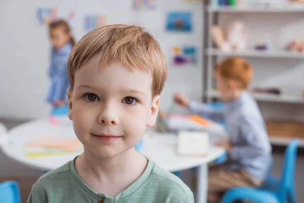 Selektiver Fokus des niedlichen kleinen Jungen, der mit Mitschülern im Klassenzimmer in die Kamera schaut — Stockfoto