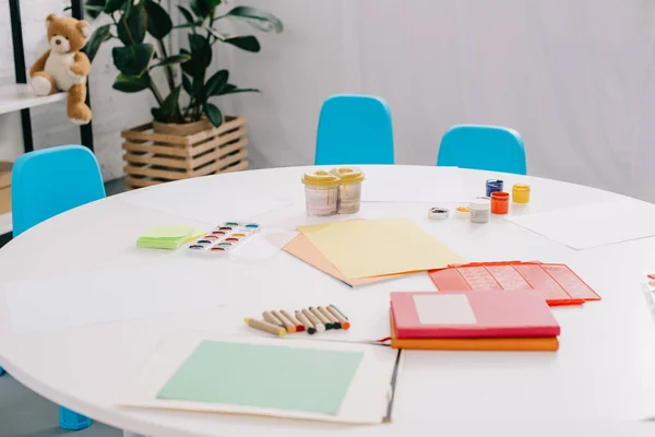 Vista de perto de papéis, tintas coloridas e lápis para desenhar na mesa em sala de aula — Fotografia de Stock
