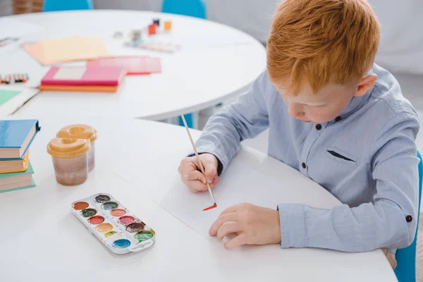 Focado pré-escolar vermelho cabelo menino desenho imagem na mesa em sala de aula — Fotografia de Stock