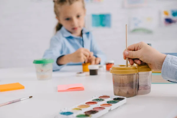 Partial view of preschoolers drawing pictures with paints and paint brushes at table in classroom — Stock Photo