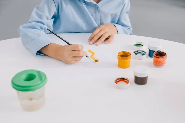 Частичный вид рисунка ребенка с красками и кистью за столом — стоковое фото