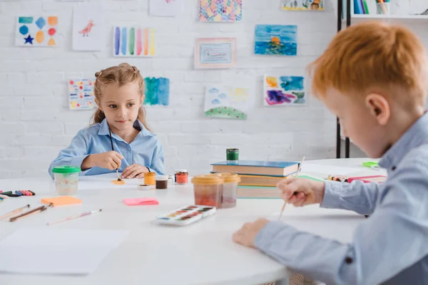 Foco seletivo de pré-escolares desenho de quadros com tintas e pincéis à mesa em sala de aula — Fotografia de Stock