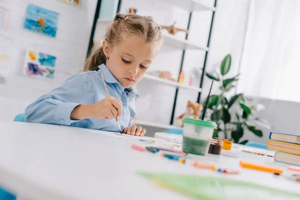 Porträt eines entzückenden fokussierten Kindes mit Farben und Pinsel am Tisch — Stockfoto
