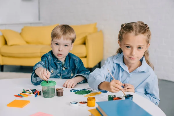 Портрет дошкольников, рисующих картины красками и кисточками за столом в классе — стоковое фото