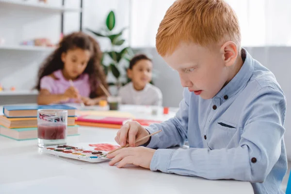Selektiver Fokus multiethnischer Kinder mit Pinseln, die Bilder im Klassenzimmer zeichnen — Stockfoto