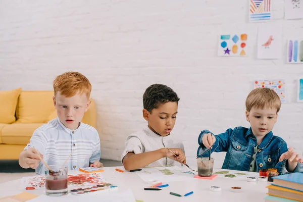 Portrait of multiethnic kids with paint brushes drawing pictures in classroom — Stock Photo