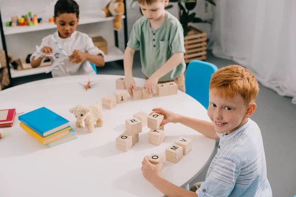 Multikulturelle kleine Jungen spielen mit Holzklötzen am Tisch im Klassenzimmer — Stockfoto