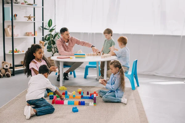 Teacher and multicultural preschoolers on floor with colorful bricks in classroom — Stock Photo