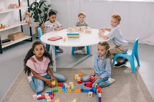 Multiracial preschoolers looking at camera while playing with wooden blocks in classroom — Stock Photo