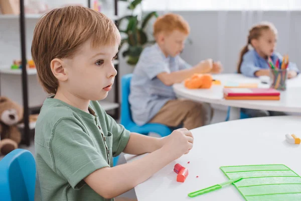 Messa a fuoco selettiva di adorabile ragazzo con plastilina seduto a tavola in aula — Foto stock