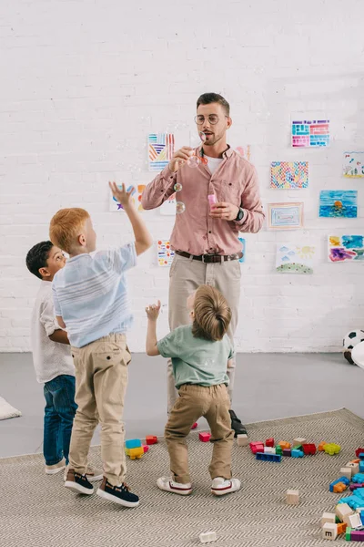 Professor soprando bolhas de sabão para meninos multirraciais em sala de aula — Fotografia de Stock