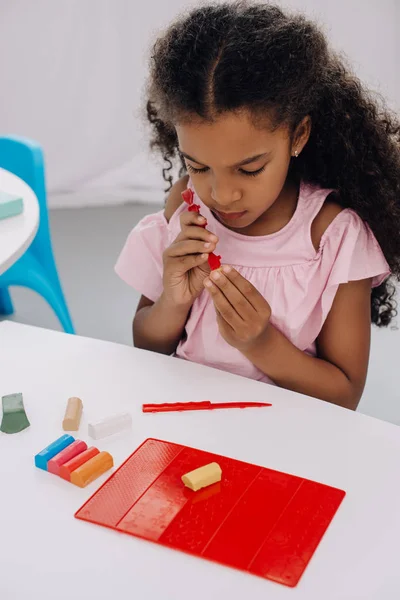 Enfant afro-américain avec plasticine dans les mains sculptant figure à table — Photo de stock