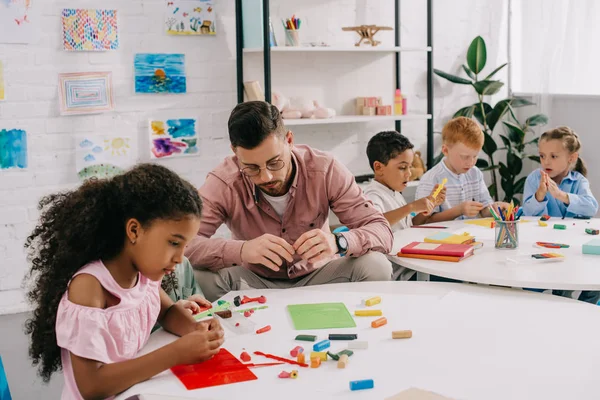 Lehrer und multiethnische Kinder gestalten Figuren mit bunter Knetmasse am Tisch im Klassenzimmer — Stockfoto