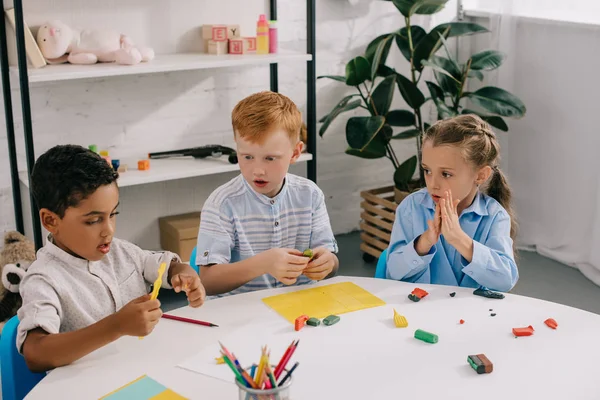 Portrait de mignons enfants d'âge préscolaire multiethnique sculptant des figures avec de la plasticine en classe — Photo de stock