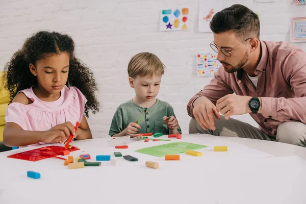 Bambini in età prescolare multietnica e insegnante con figure scultoree in plastilina a tavola in aula — Foto stock