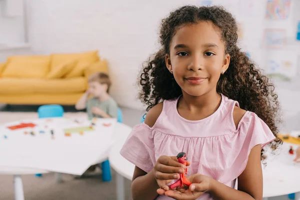Foyer sélectif de l'enfant afro-américain avec plasticine dans les mains et camarade de classe caucasien derrière dans la salle de classe — Photo de stock