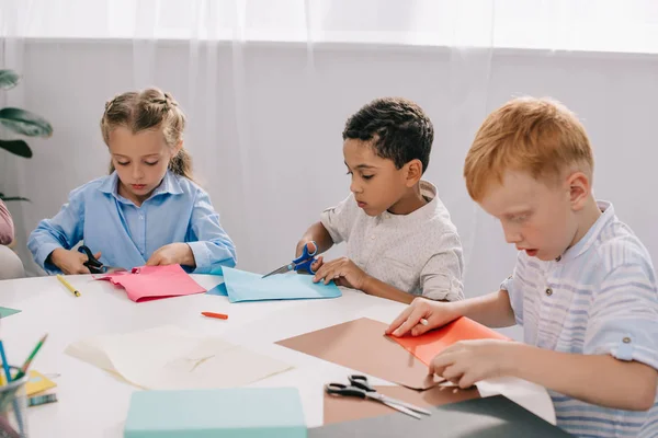 Focused multicultural kids making paper applique in classroom — Stock Photo