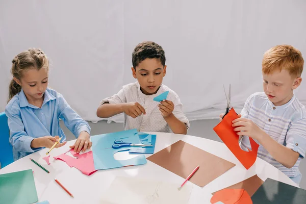 Зосереджені багаторасові діти роблять паперову аплікацію в класі — стокове фото