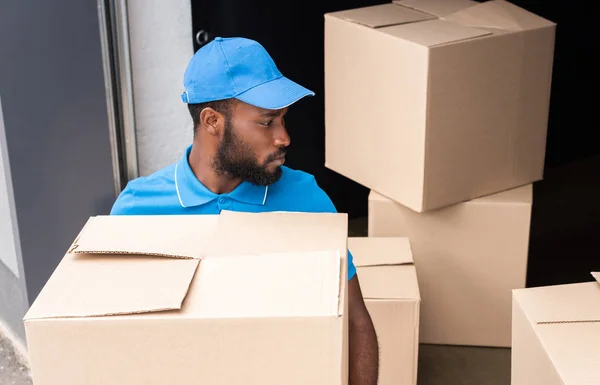 Vue grand angle du livreur afro-américain tenant la boîte près du stockage — Photo de stock