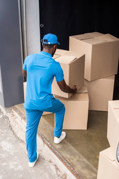 Visão traseira do homem de entrega afro-americano colocando caixas na pilha — Fotografia de Stock