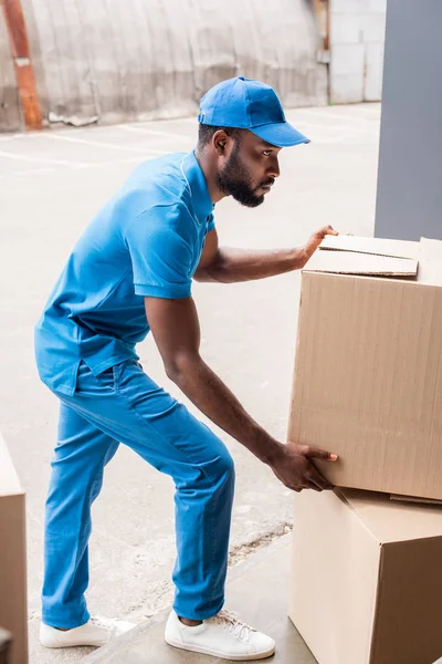 Vue latérale du livreur afro-américain mettant des boîtes sur pilotis — Photo de stock