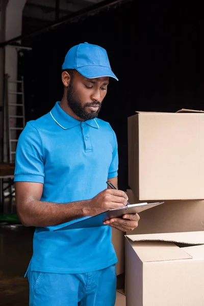 Mensajero afroamericano escribiendo algo al portapapeles - foto de stock