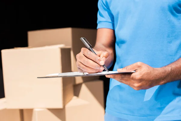 Cropped image of african american delivery man writing something to clipboard — Stock Photo