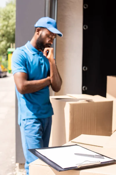 Афроамериканський чоловік доставки дивиться на коробки з буферами і ручкою на передньому плані — стокове фото