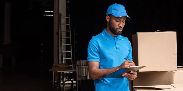 Afrikanischer amerikanischer Zusteller schreibt etwas in Klemmbrett — Stockfoto