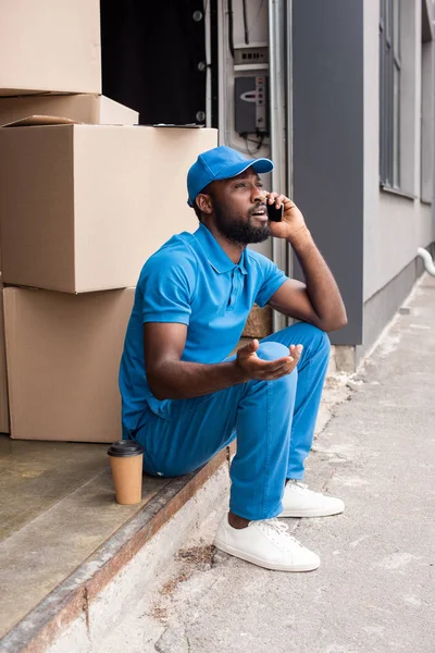 Afro-américain livraison homme gesticuler et parler par smartphone — Photo de stock