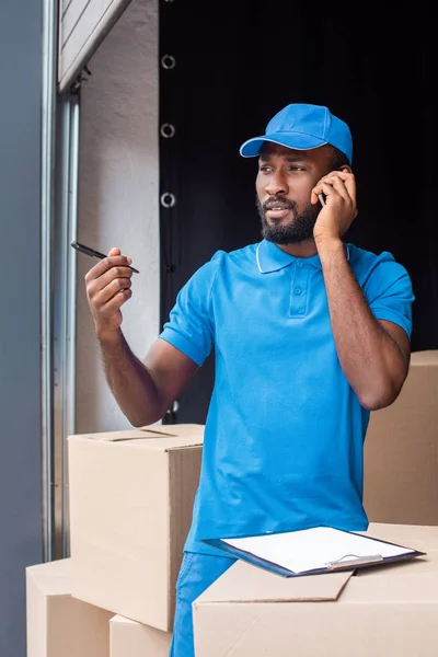 Africano americano repartidor hombre hablando por teléfono inteligente y mirando hacia otro lado - foto de stock