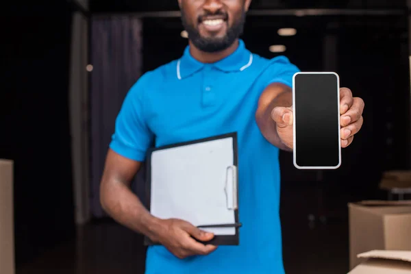 Immagine ritagliata dell'uomo africano americano di consegna che mostra smartphone con schermo bianco — Foto stock