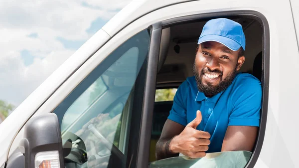 Sonriente afroamericano repartidor mostrando el pulgar hacia arriba de van - foto de stock