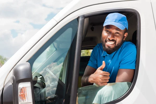 Sonriente afroamericano repartidor mostrando el pulgar hacia arriba desde el coche - foto de stock