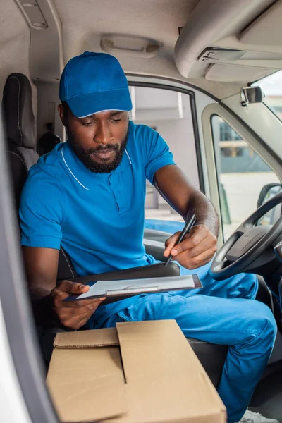 Africano americano entrega homem segurando prancheta e caneta em van — Fotografia de Stock
