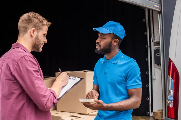 African american courier counting cost of delivery, client writing to clipboard — Stock Photo