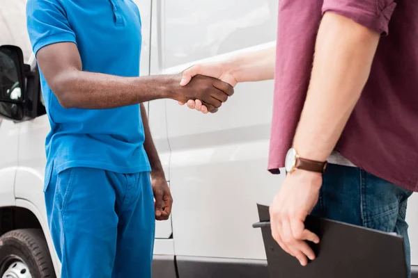Cropped image of multicultural courier and client shaking hands near van — Stock Photo