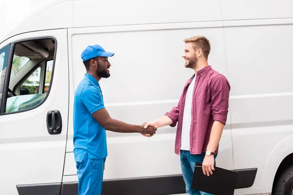 Side view of multicultural courier and client shaking hands near van — Stock Photo