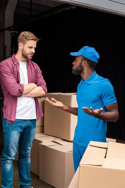 Cliente caucásico con brazos cruzados mirando al mensajero afroamericano - foto de stock