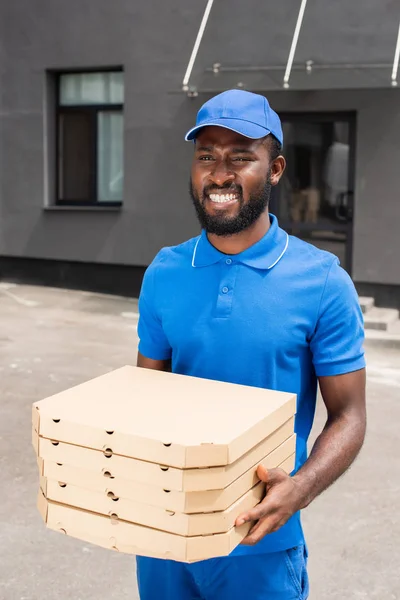 Repartidor afroamericano sonriente sosteniendo cajas de pizza - foto de stock