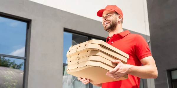 Низький кут зору усміхненого кавказького кур'єра з коробками для піци — стокове фото
