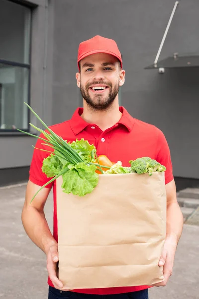 Sourire caucasien livreur tenant sac en papier avec des légumes — Photo de stock