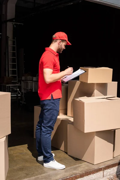 Vue latérale du livreur en uniforme notes de contrôle dans le bloc-notes — Photo de stock