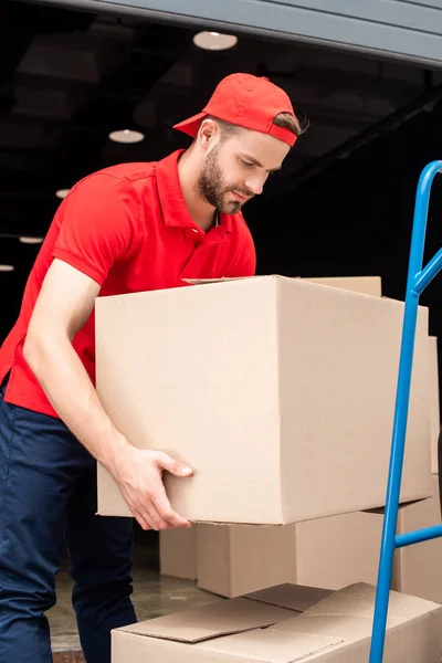 Vue latérale du livreur mettant des boîtes en carton sur le chariot de livraison — Photo de stock