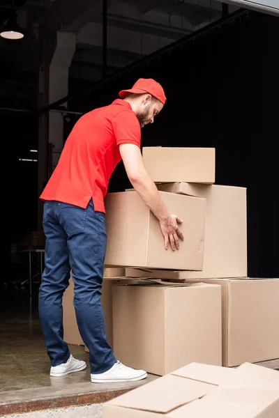 Joven repartidor en uniforme rojo con cajas de cartón - foto de stock