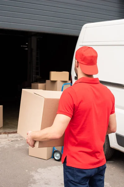 Visão traseira do entregador em uniforme vermelho que transporta a carga — Fotografia de Stock