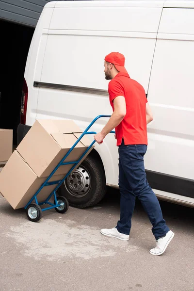 Vista lateral del hombre de entrega con cajas de cartón en el carrito de entrega - foto de stock