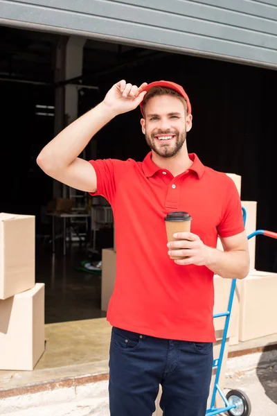 Ritratto di allegro fattorino con caffè da portare a mano e carico alle spalle — Foto stock